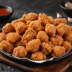Premium fried chicken hot shots served on a black plate with crispy golden coating and dipping sauce.