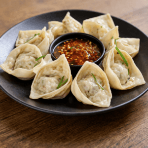 Unfried chicken wontons arranged on a black plate with dipping sauce, raw dumplings filled with minced chicken and herbs
